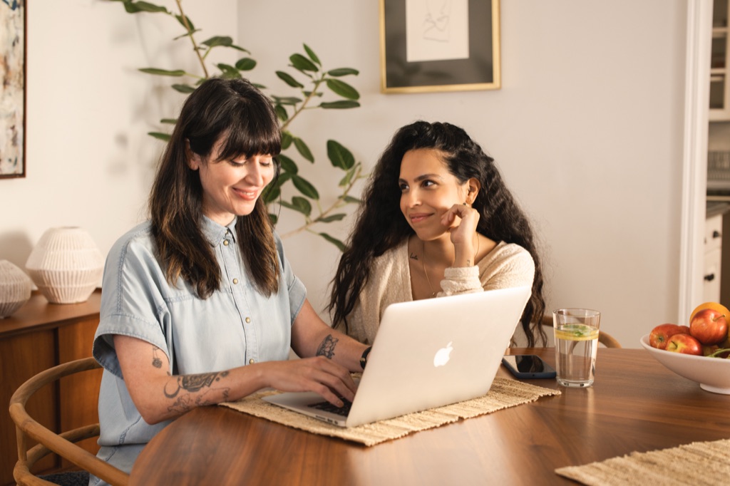 Woman smiling warmly at her partner as she types on a laptop at the dining table, photographed by Dawn Heumann