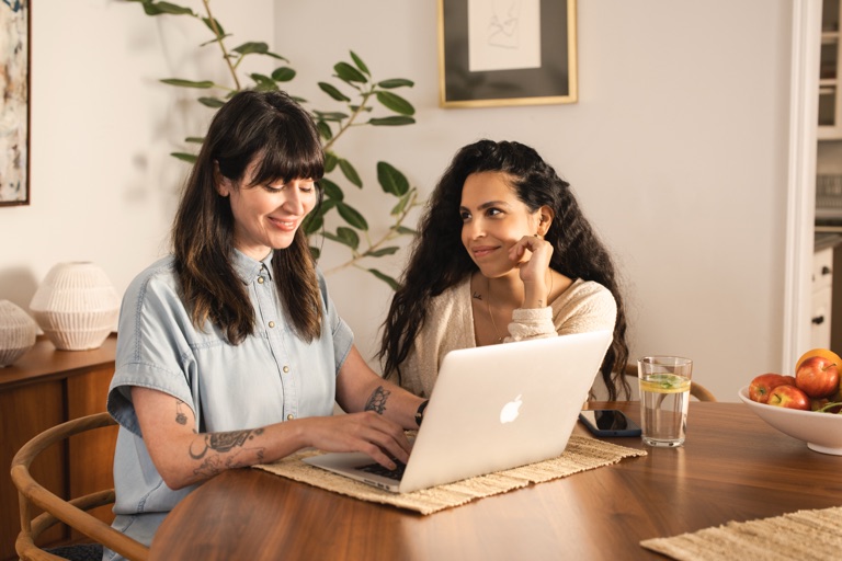 Woman smiling warmly at her partner as she types on a laptop at the dining table, photographed by Dawn Heumann