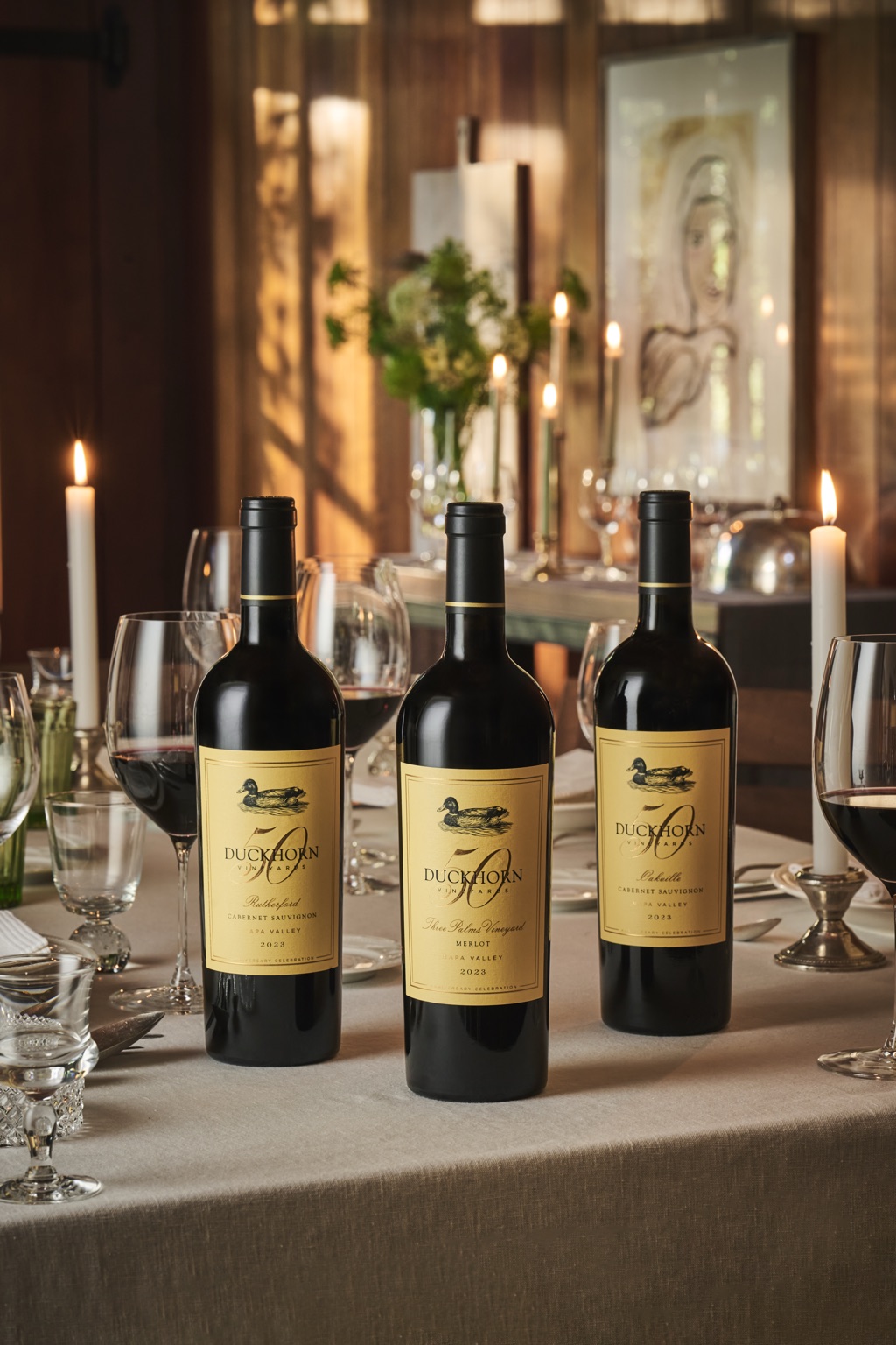 Three Duckhorn Vineyards 50th anniversary bottles, Rutherford Cabernet, Three Palms Vineyard Merlot, and Oakville Cabernet, on a candlelit table