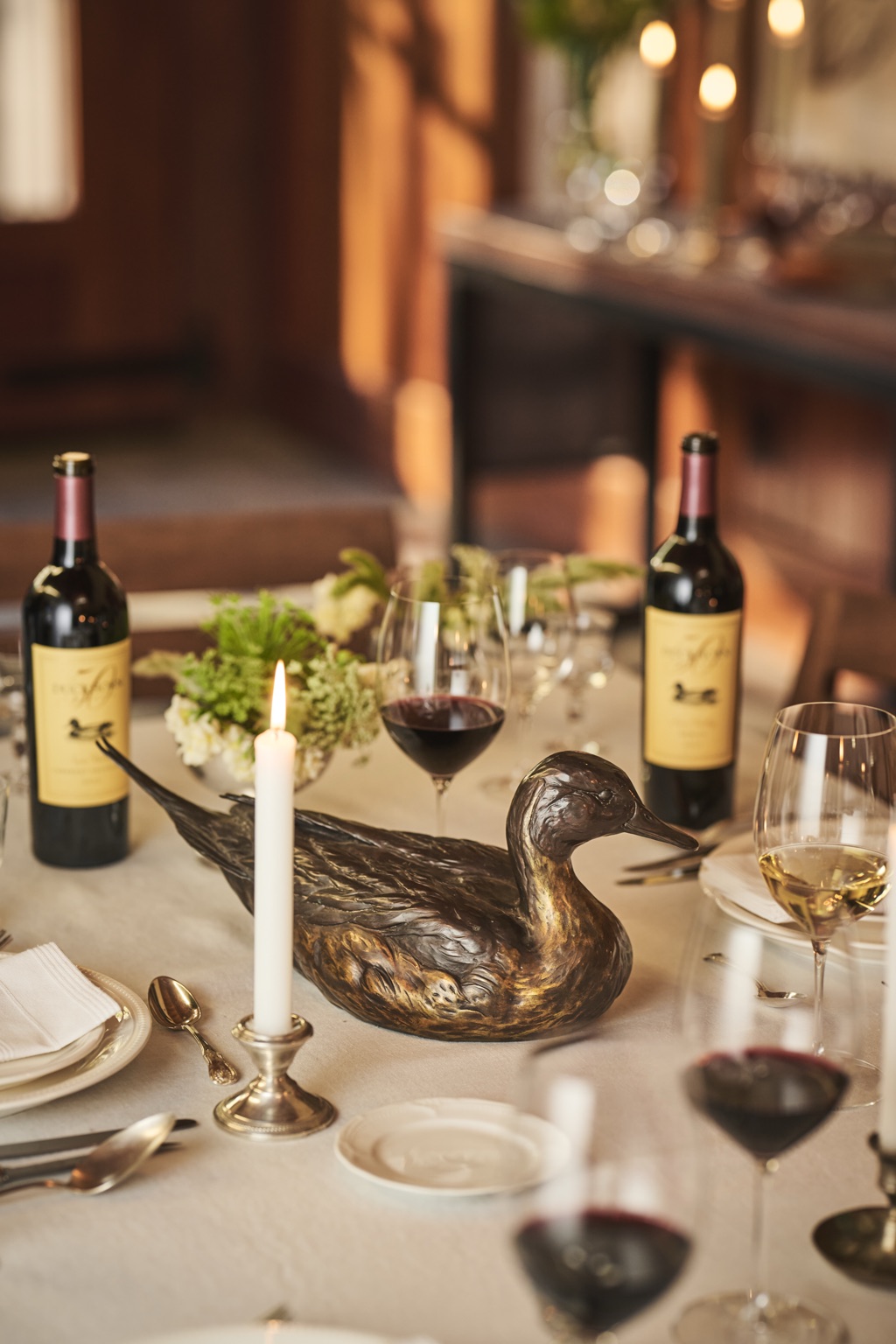 Bronze duck centerpiece on a candlelit anniversary dinner table between two bottles of Duckhorn wine