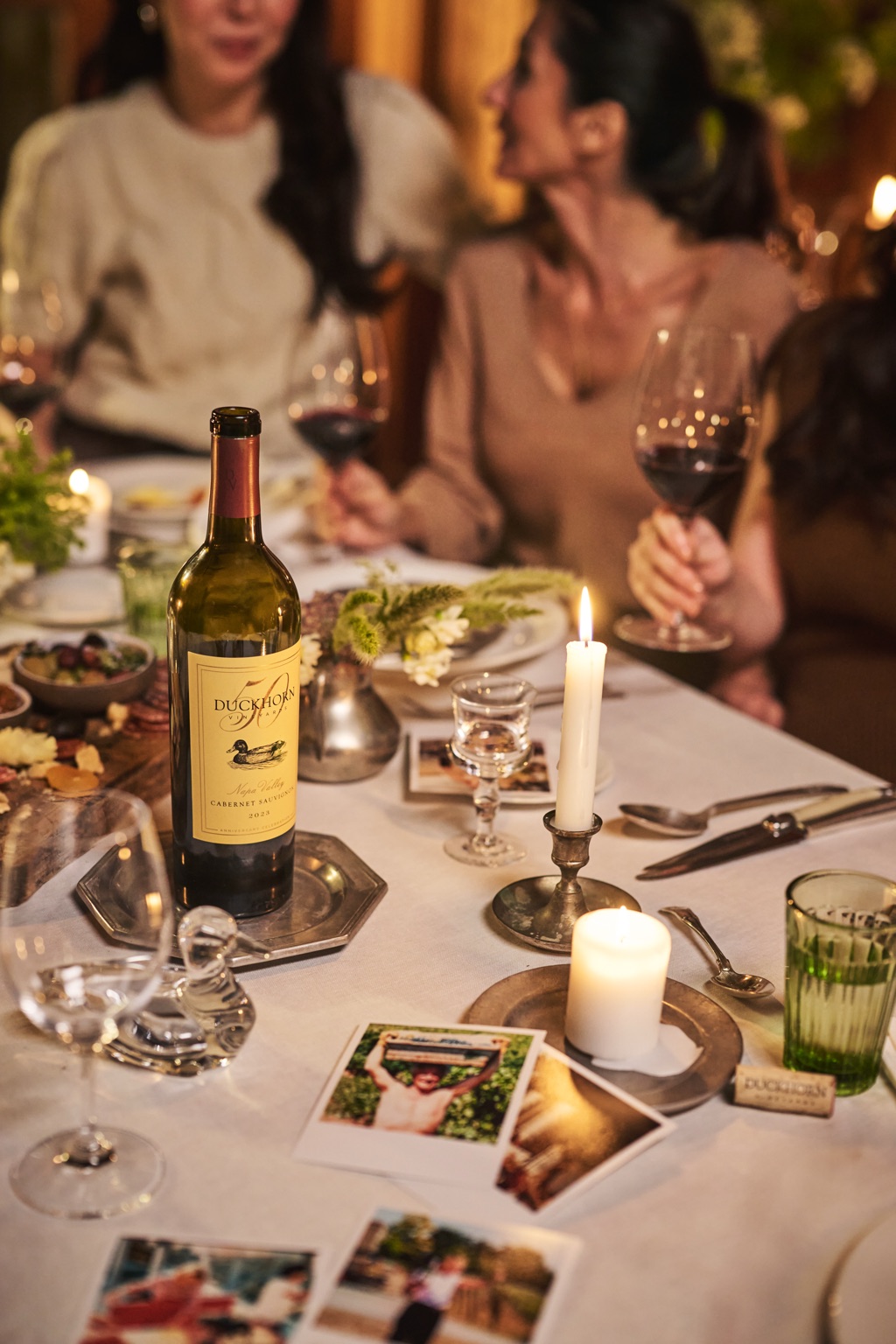 Duckhorn 50th anniversary Napa Valley Cabernet on the table with old polaroids, a wine cork, and a glass duck