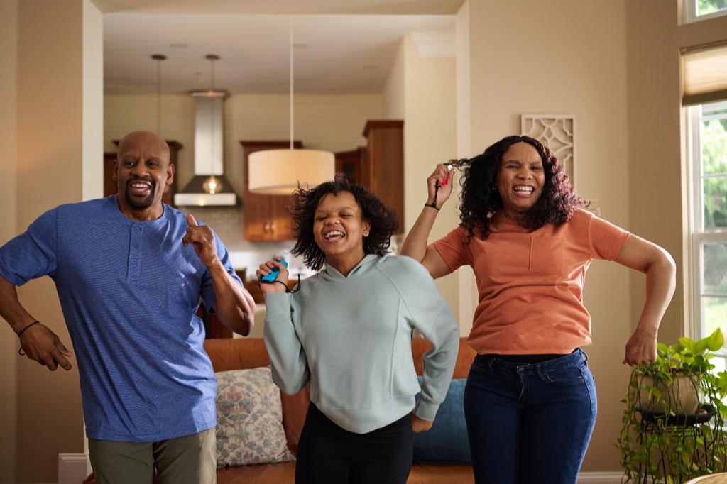 Family of three dancing together with game controllers in hand during a living room dance game