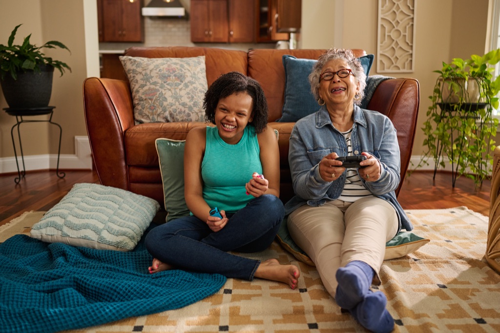 Grandmother and granddaughter laughing with game controllers on the living room floor