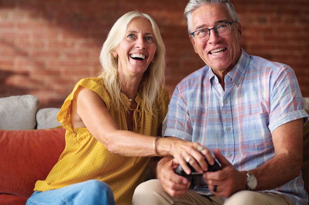Older couple laughing as she playfully grabs his game controller mid-match