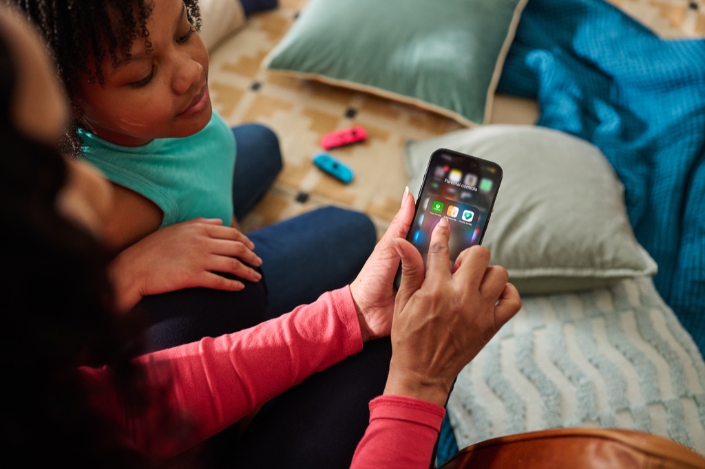 Mother showing her daughter a parental controls folder of family safety apps on her phone