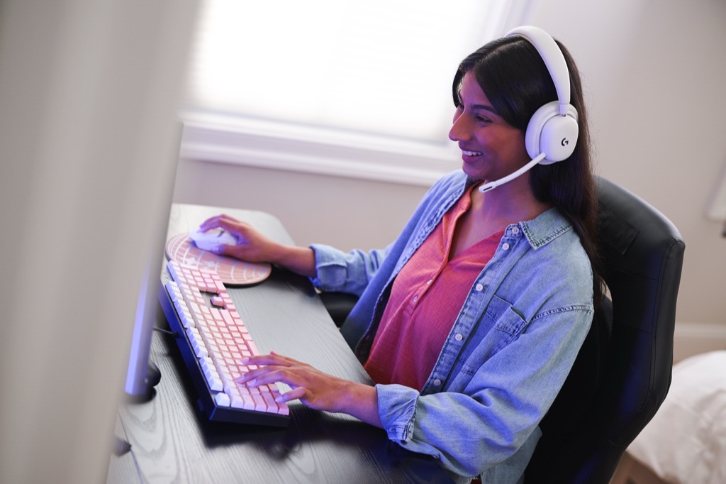 Woman in a white gaming headset smiling at her PC with a pink mechanical keyboard