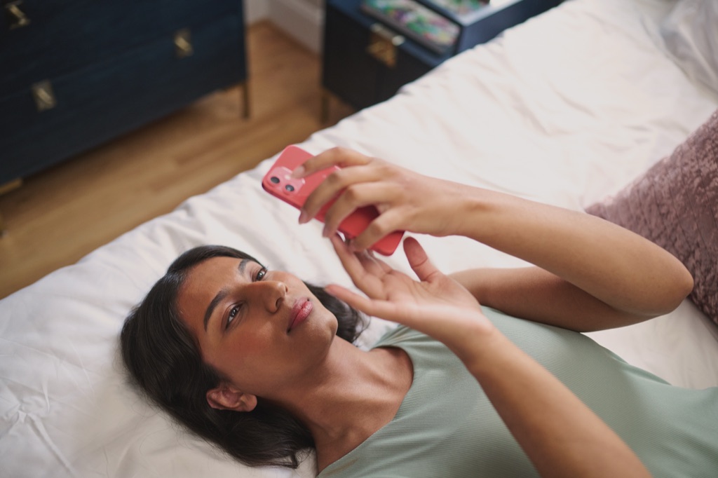 Teen lying back on her bed playing a game on her phone