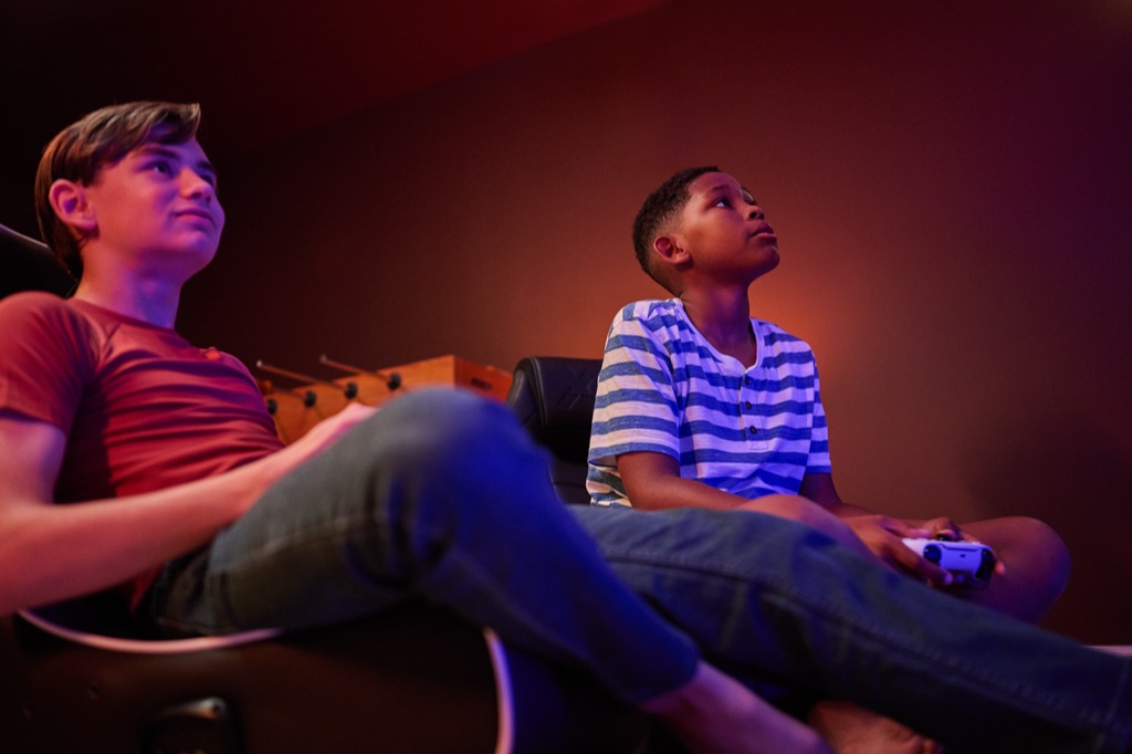 Low angle of two teenage boys playing a console game together in warm low light, photographed by Dawn Heumann