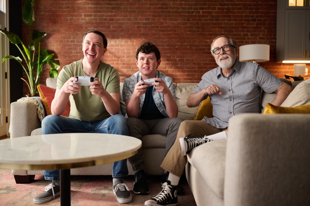 Dad, teenage son, and grandfather playing a video game together on the couch