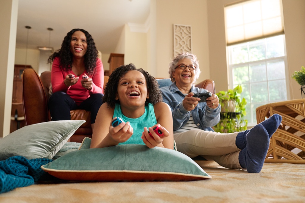 Girl playing a video game on the floor while her mom and grandmother cheer from the couch