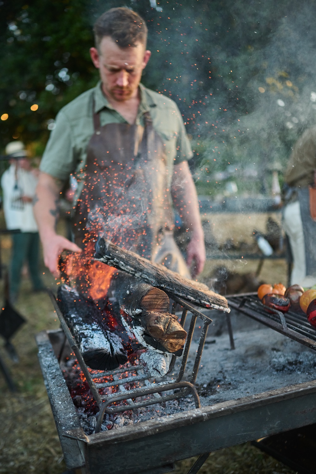 Chef laying a log on the fire as sparks and smoke swirl above the grill