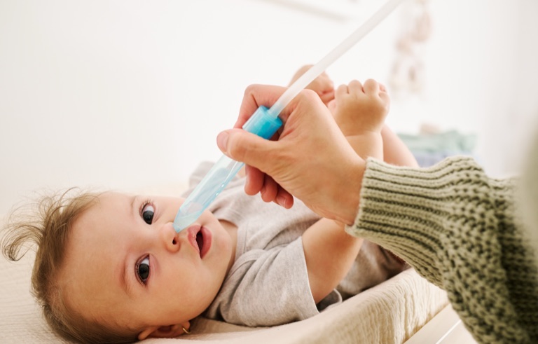 Parent giving a baby saline nose drops on a changing pad, photographed for Frida Baby by Dawn Heumann