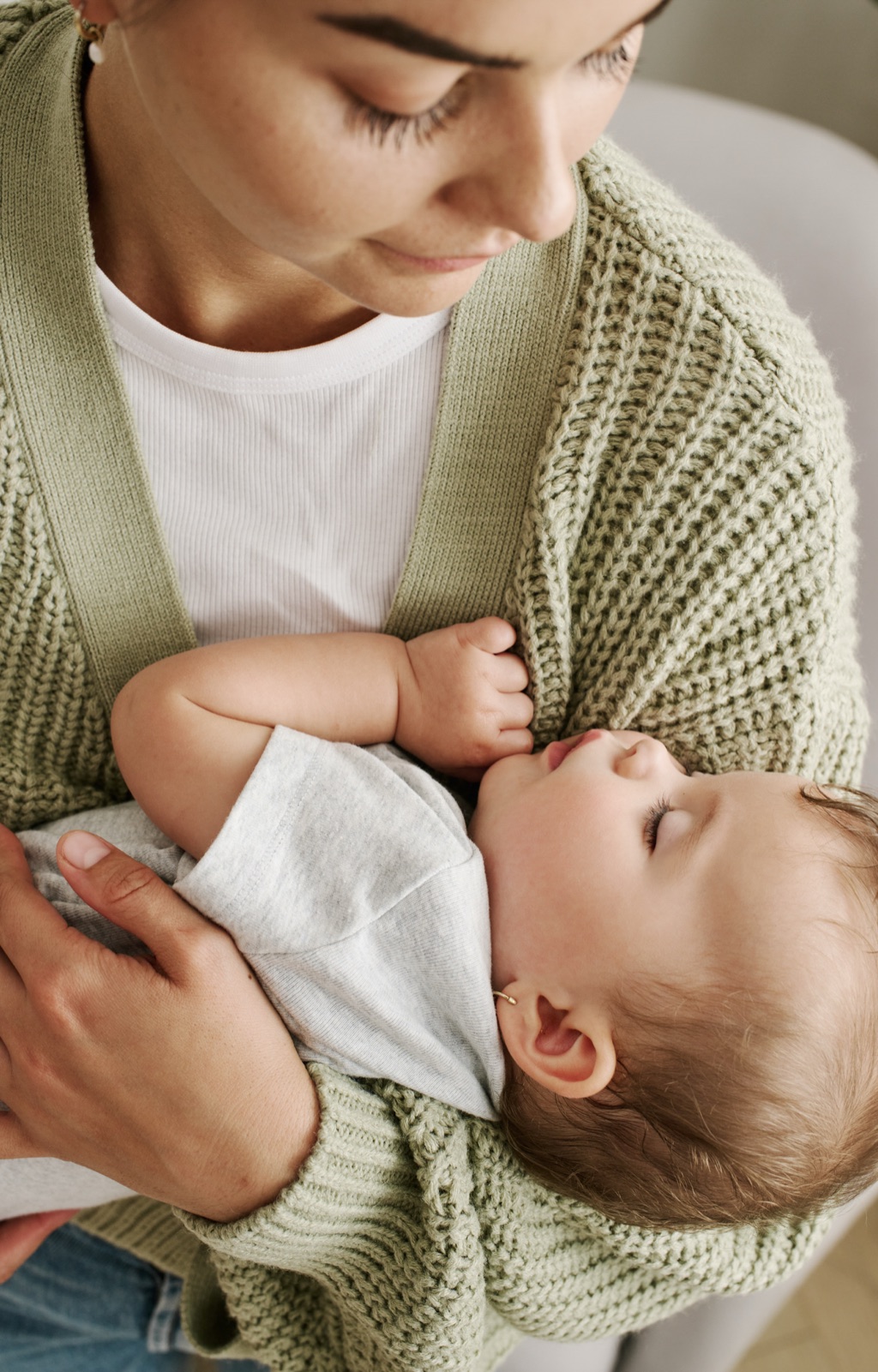 Mother in a sage cardigan cradling her sleeping newborn, Frida campaign lifestyle photography