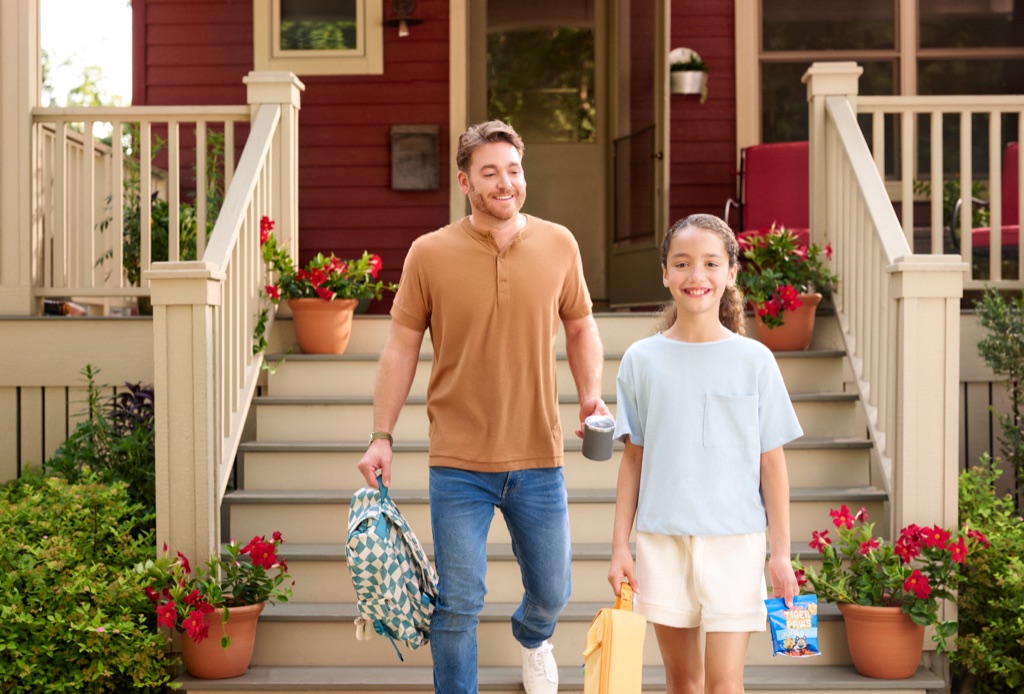 Dad and daughter heading down the front porch steps on a school morning with backpack and Kellogg's Tiger Paws snack