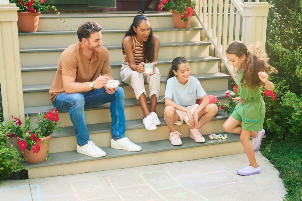 Family of four having breakfast on the front steps while the youngest plays hopscotch, Kellogg's campaign photography by Dawn Heumann