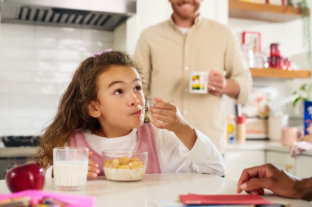Girl eating Corn Flakes at the kitchen counter while dad looks on, Kellogg's campaign photography by Dawn Heumann