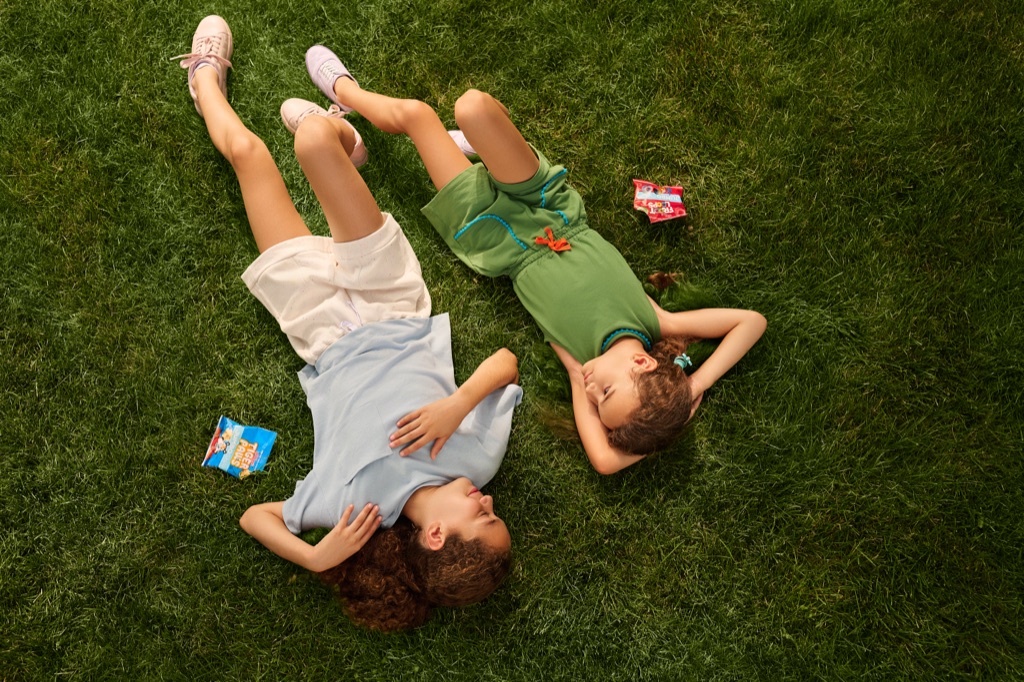 Overhead of two girls lying in the grass with Kellogg's Tiger Paws and Froot Loops Jumbo Snax, photographed by Dawn Heumann