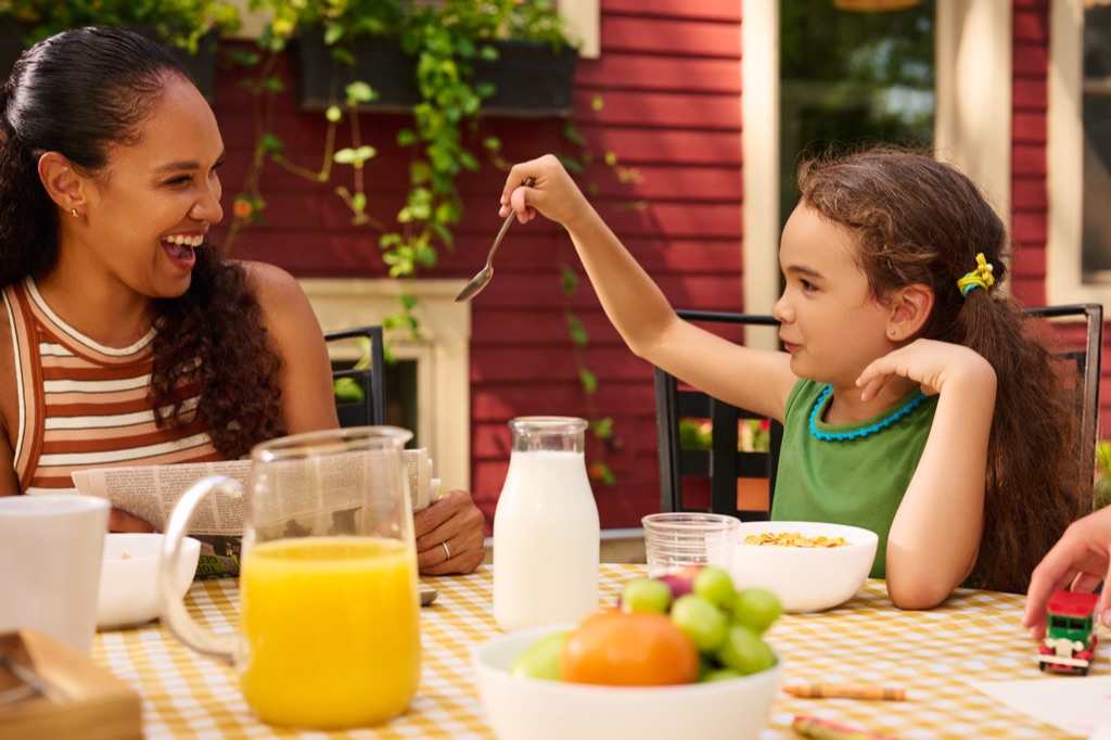 Mom laughing with her daughter over cereal at an outdoor breakfast table, Kellogg's campaign photography by Dawn Heumann