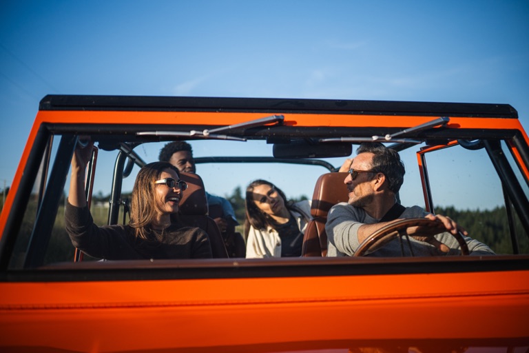 Four friends inside a restored orange vintage Ford Bronco seen through the windshield, photographed for Kindred by Dawn Heumann