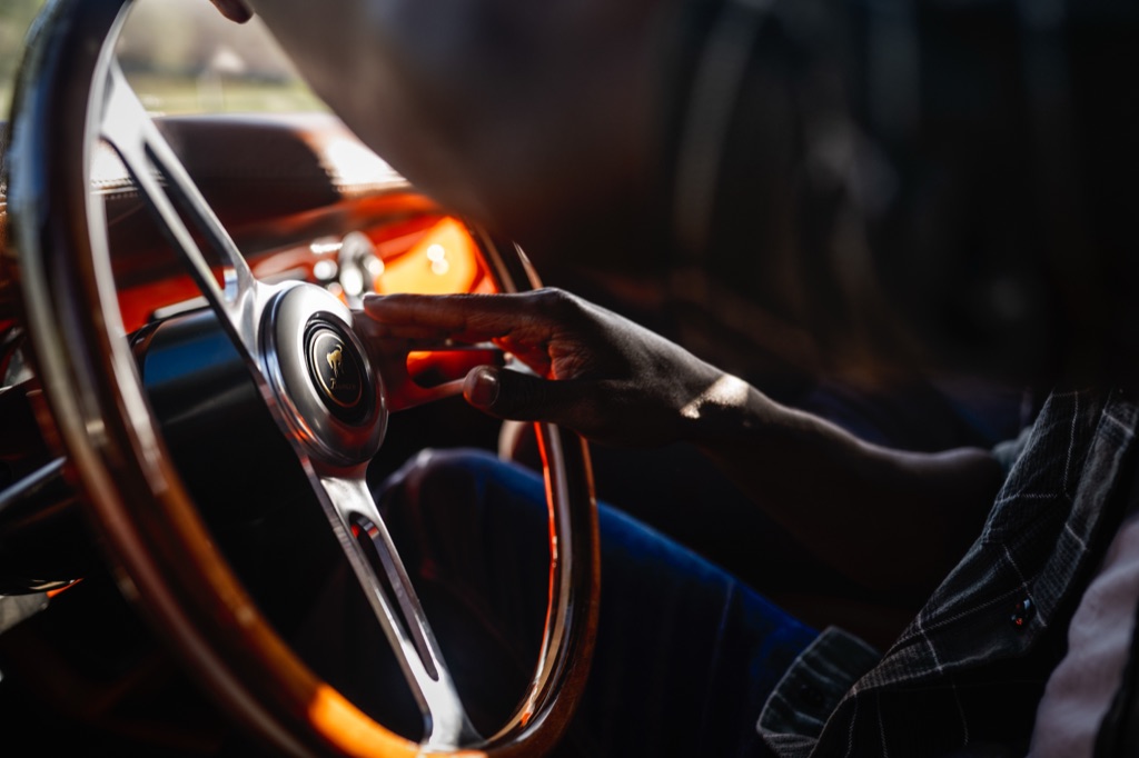 Detail of a hand on the wood-rimmed steering wheel and Bronco horn button of a restored Ford Bronco