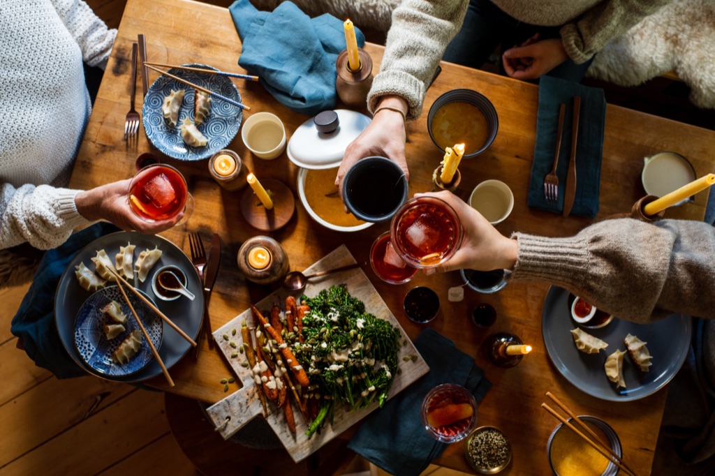 Overhead of friends toasting negronis over a candlelit table of dumplings, roasted carrots, and broccolini
