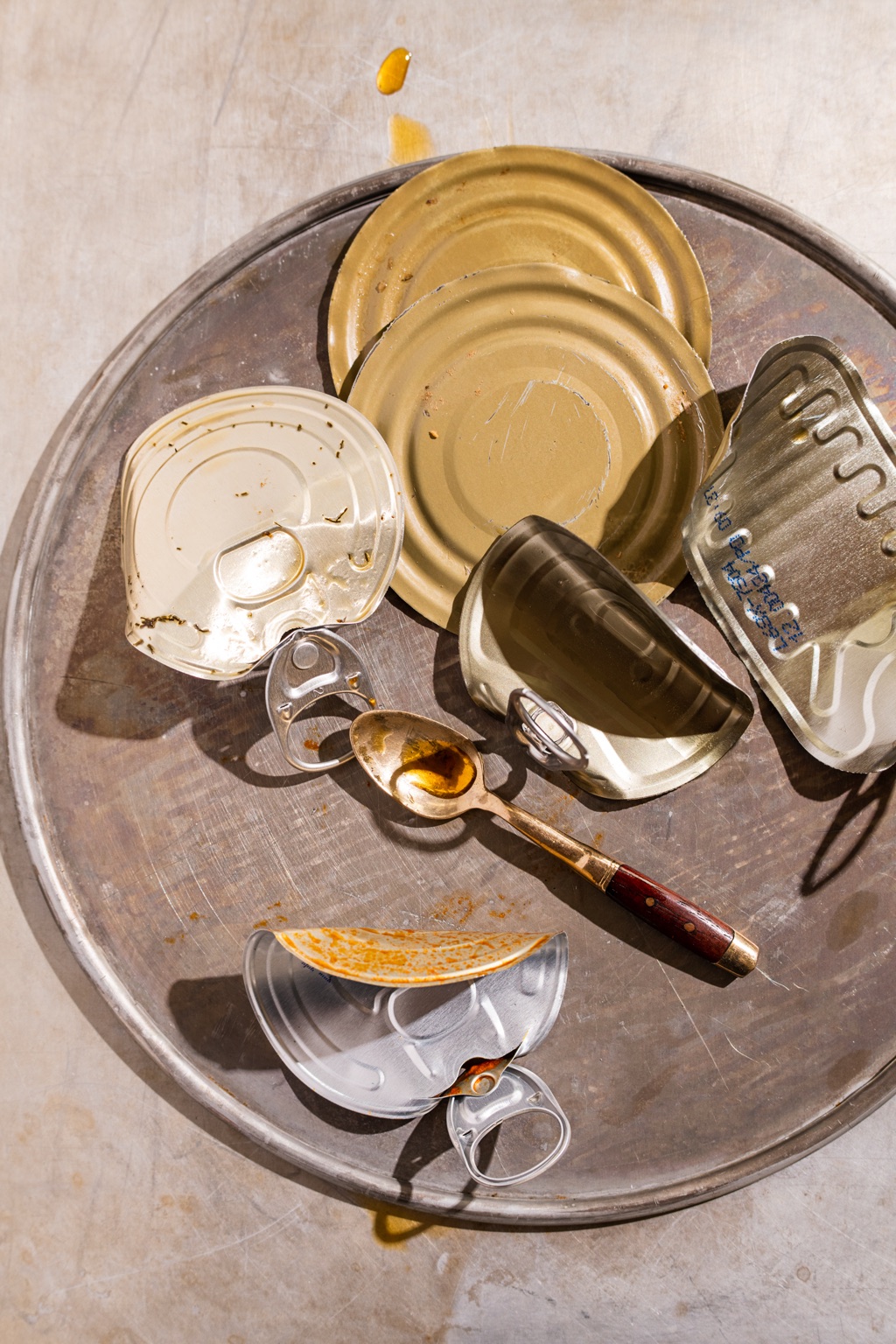 Still life of empty seafood tin lids and a spoon on a scratched metal tray
