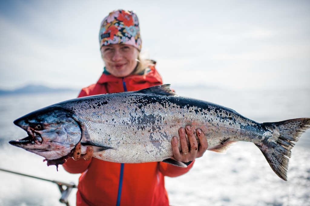 Woman in a floral beanie and red jacket holding a large king salmon up to the camera in Alaska