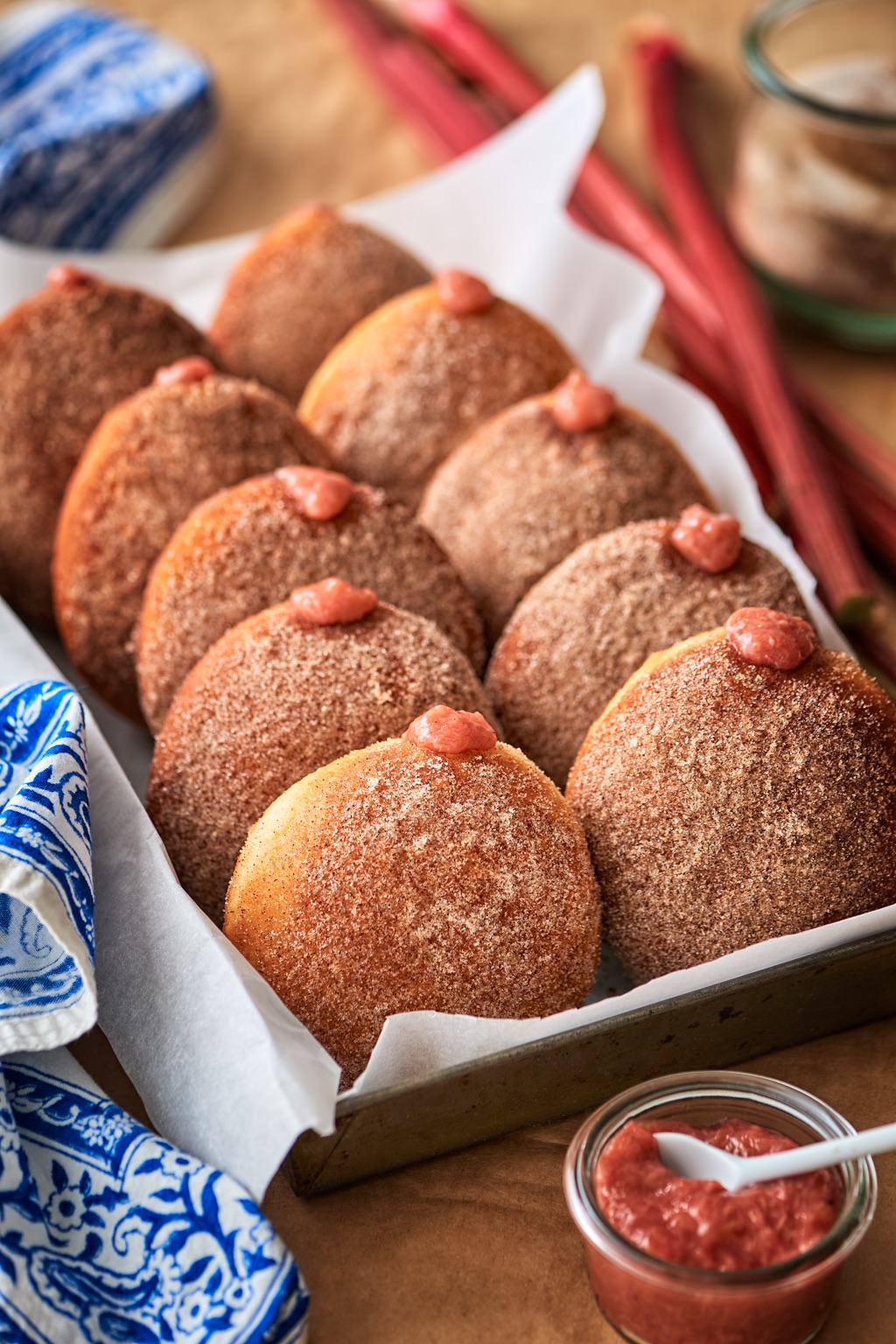 Tray of cinnamon sugar doughnuts piped with rhubarb compote, fresh rhubarb stalks behind