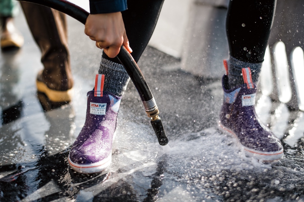 Hosing off purple XtraTuf Salmon Sisters ankle boots on a wet boat deck