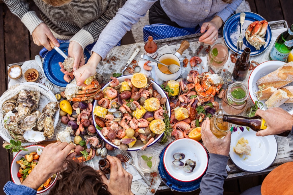 Overhead of the table mid-feast as one guest shucks an oyster and another pours a beer over the seafood boil, photographed in Alaska