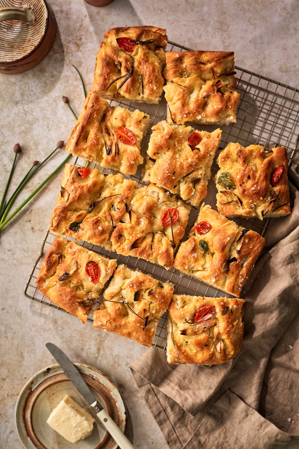 Squares of cherry tomato and spring onion focaccia with flaky salt on a wire cooling rack