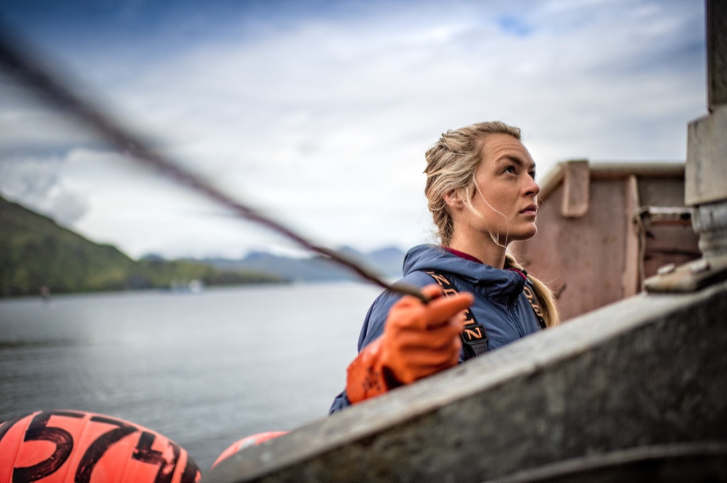 Woman in orange rubber gloves working lines aboard a fishing boat with orange buoys