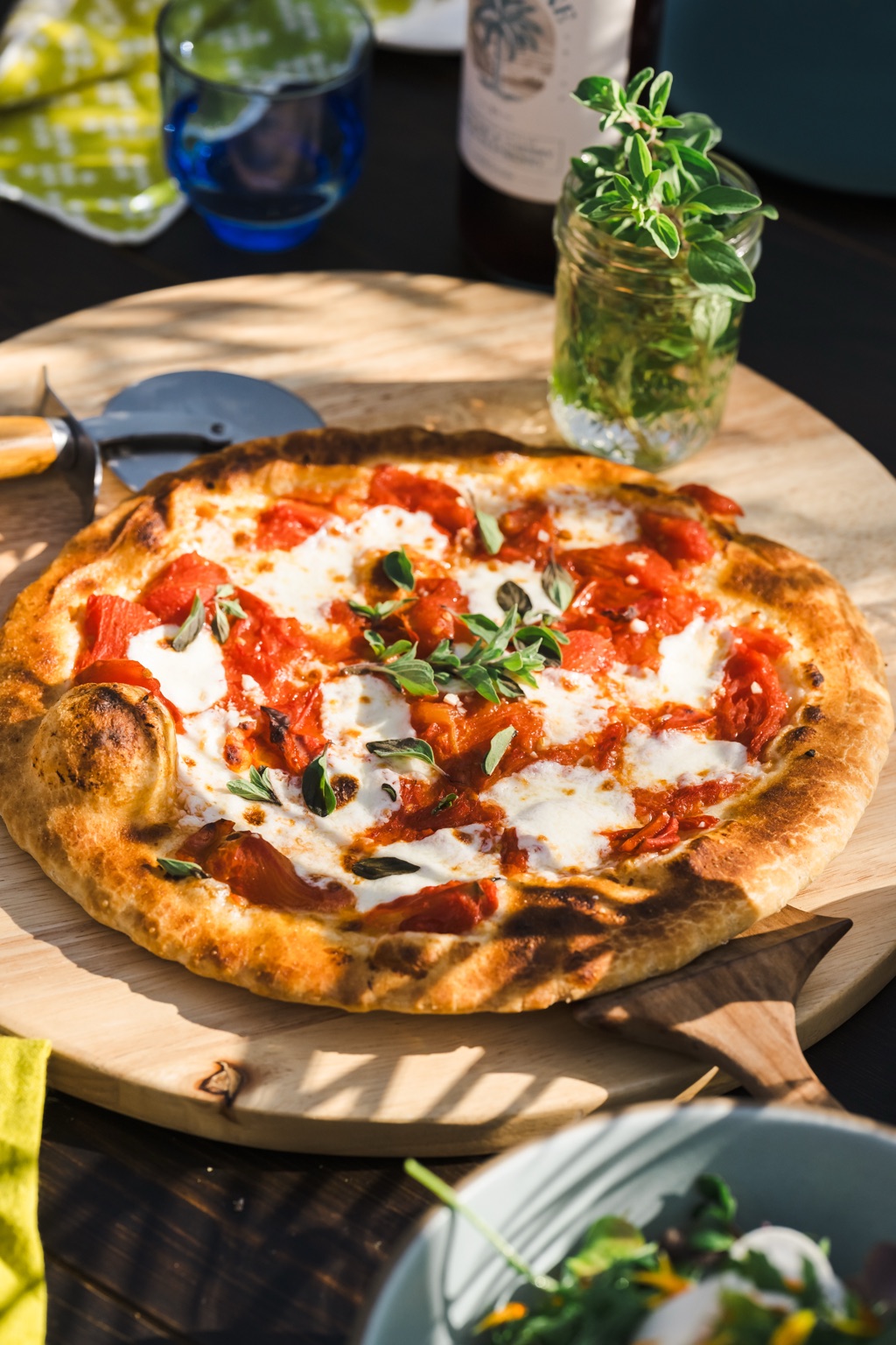 Wood-fired margherita pizza on an outdoor table with fresh oregano and a bottle of Ranch Wine, al fresco entertaining photography