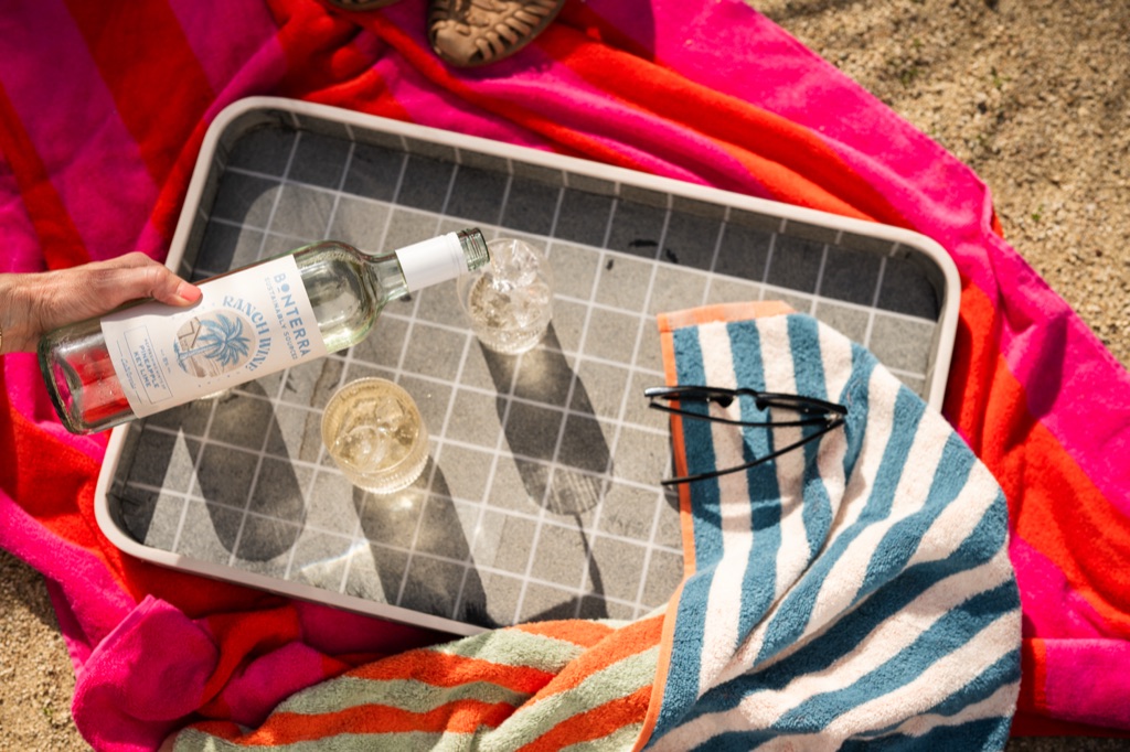 Overhead of a Ranch Wine Pineapple Key Lime pour over ice on a tiled tray set on bright striped beach towels
