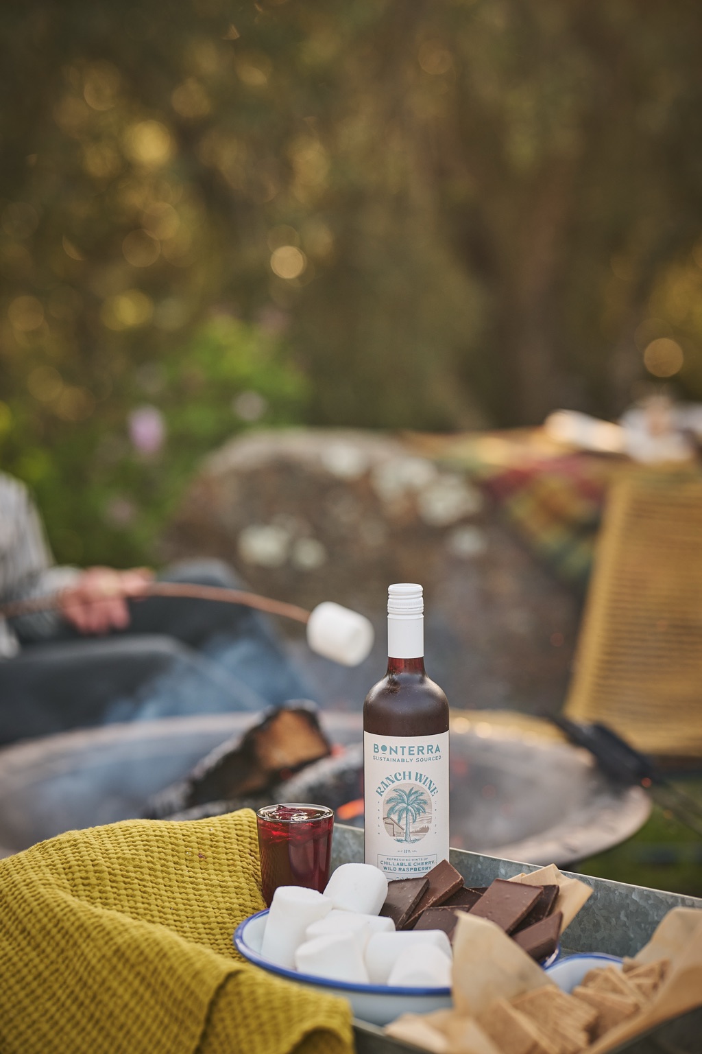 Bottle of Ranch Wine Chillable Cherry Wild Raspberry beside a s'mores tray while a marshmallow toasts over the fire pit, photographed by Dawn Heumann