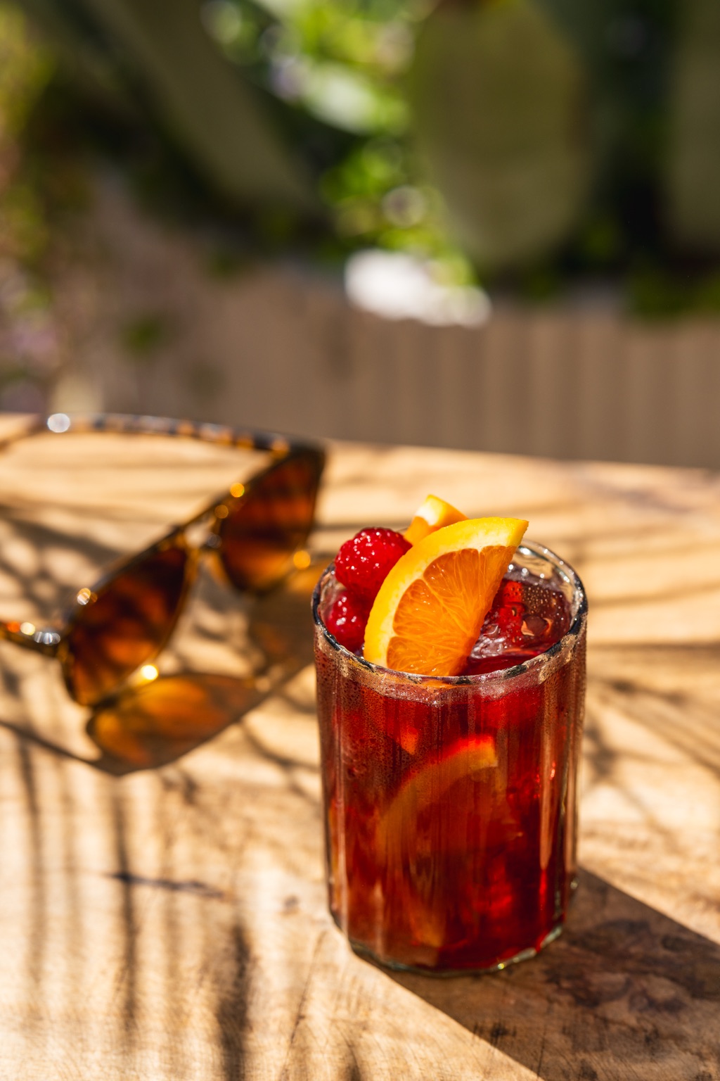 Cherry wild raspberry wine spritz in a ribbed glass with an orange slice and fresh raspberries in dappled sunlight