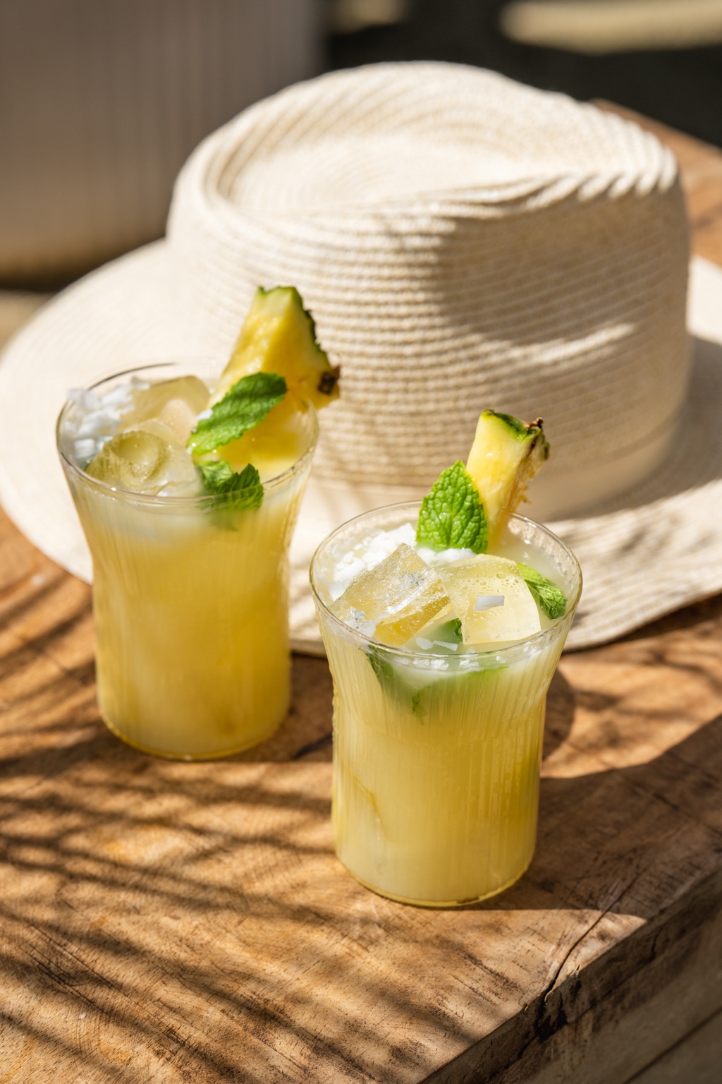 Two pineapple key lime wine cocktails with mint, pineapple wedges, and toasted coconut beside a straw hat