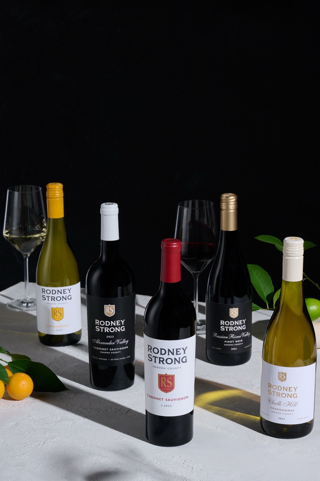 Five Rodney Strong bottles arranged diagonally against a black backdrop with kumquats and citrus leaves