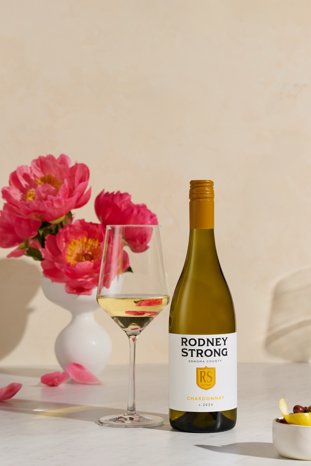 Rodney Strong Sonoma County Chardonnay with a glass and coral peonies on marble
