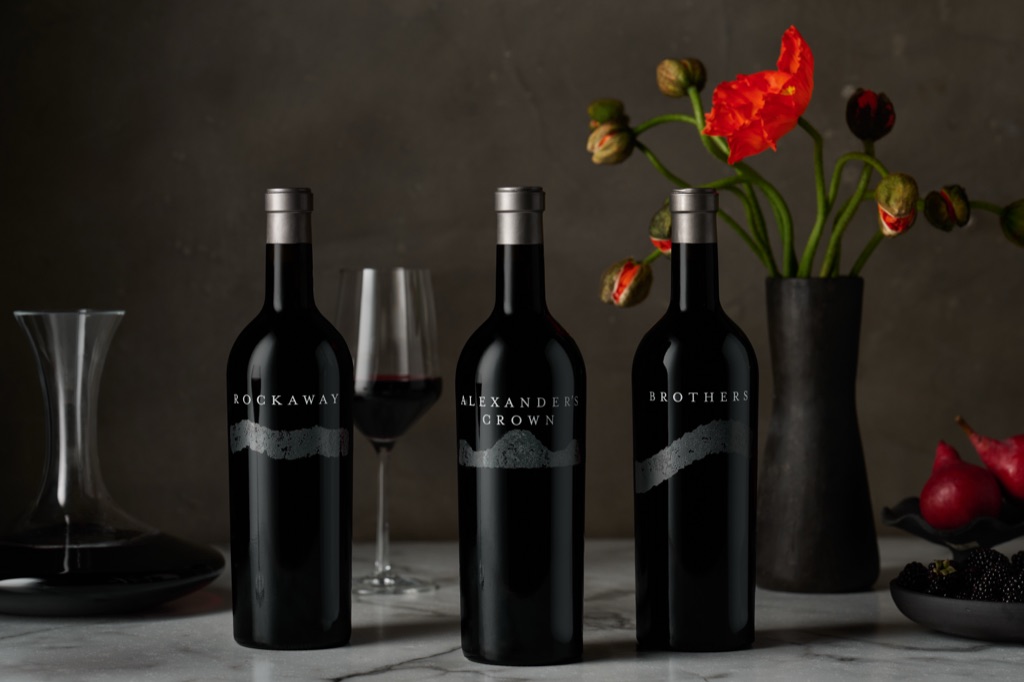Rockaway, Alexander's Crown, and Brothers single vineyard bottles in dramatic light with red poppies and a decanter, photographed by Dawn Heumann