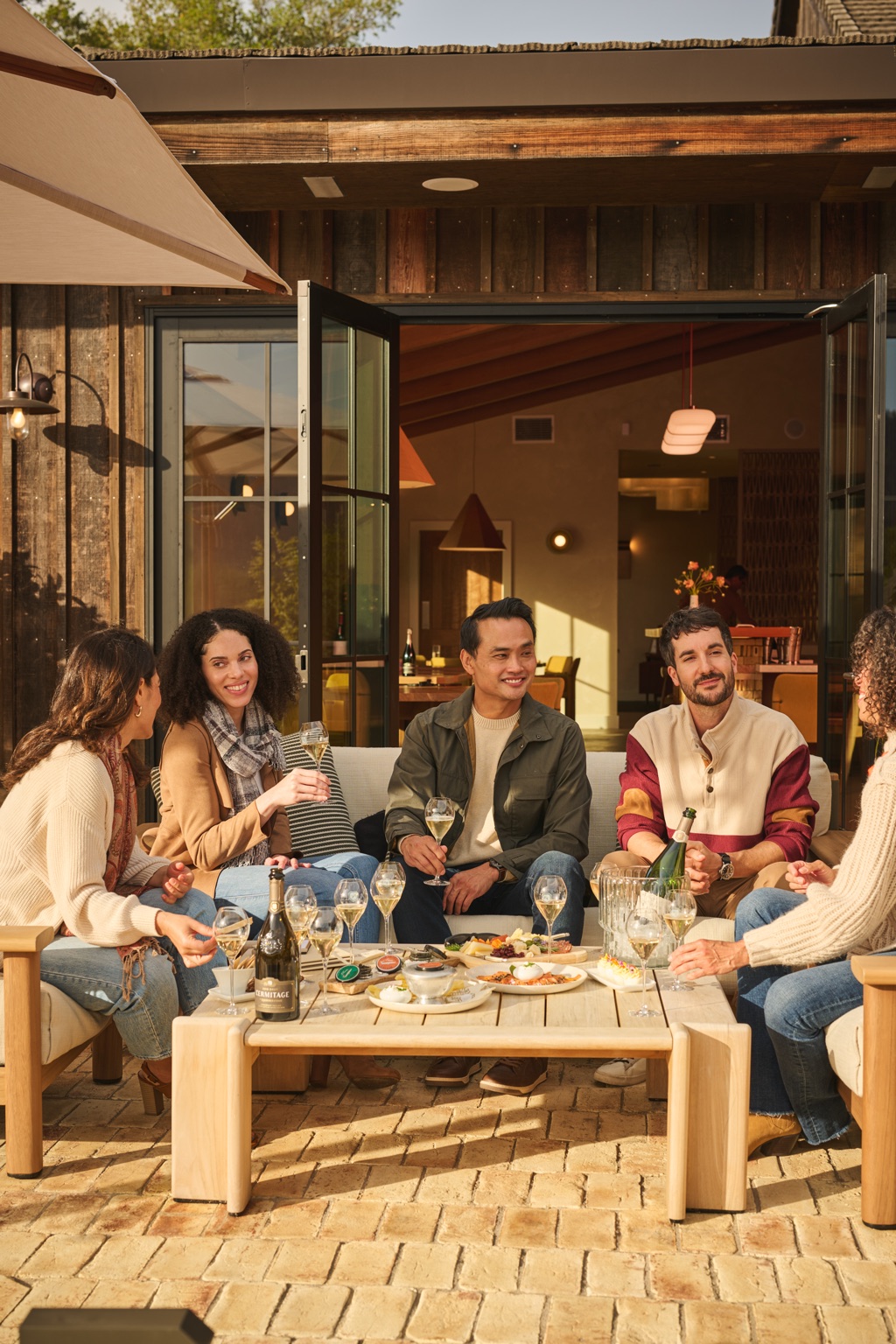 Friends gathered around a tasting spread on the courtyard patio outside the open tasting room doors