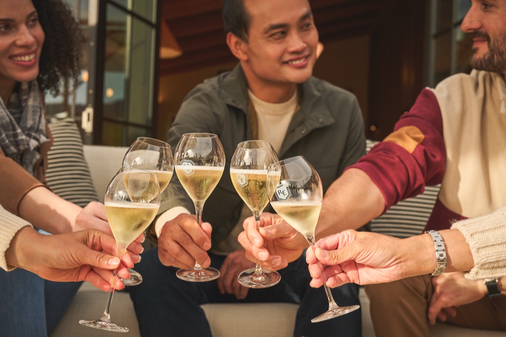 Close-up of five friends clinking etched Roederer Estate glasses of sparkling wine