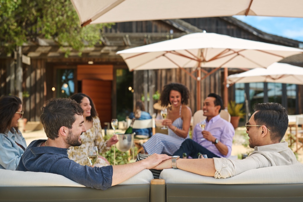 Friends relaxing with glasses of sparkling wine under cream umbrellas on the winery patio