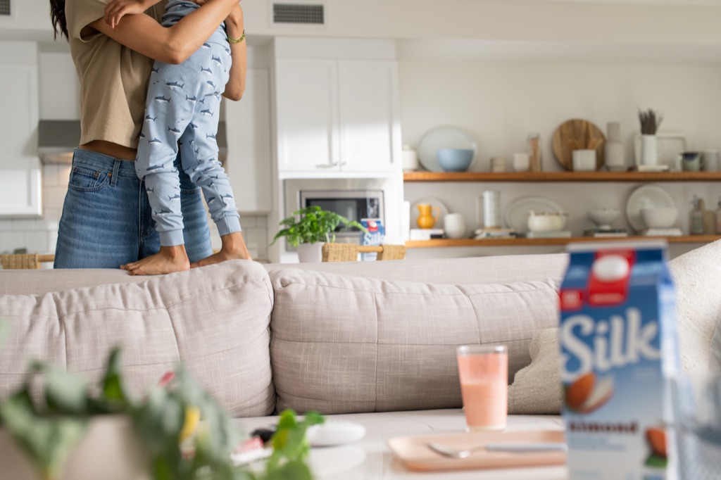 Mom scooping up her son in the kitchen with Silk almondmilk on the shelf