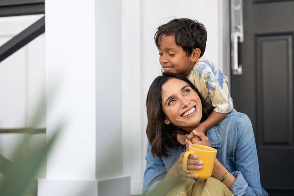 Son hugging mom from behind on the porch, yellow mug in hand, Silk campaign photography by Dawn Heumann