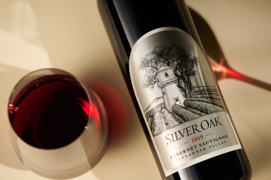 Silver Oak 2019 Alexander Valley Cabernet Sauvignon beside a glass of red wine on a warm cream backdrop, beverage photography by Dawn Heumann
