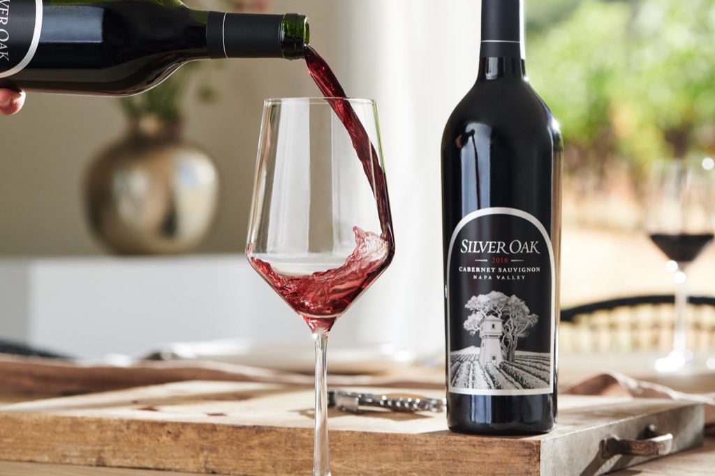Red wine pouring into a glass beside a bottle of Silver Oak Napa Valley Cabernet Sauvignon
