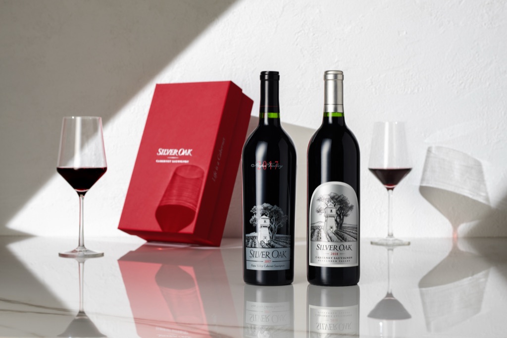 Silver Oak 2017 Napa Valley and 2018 Alexander Valley cabernets with a red gift box and two glasses on marble