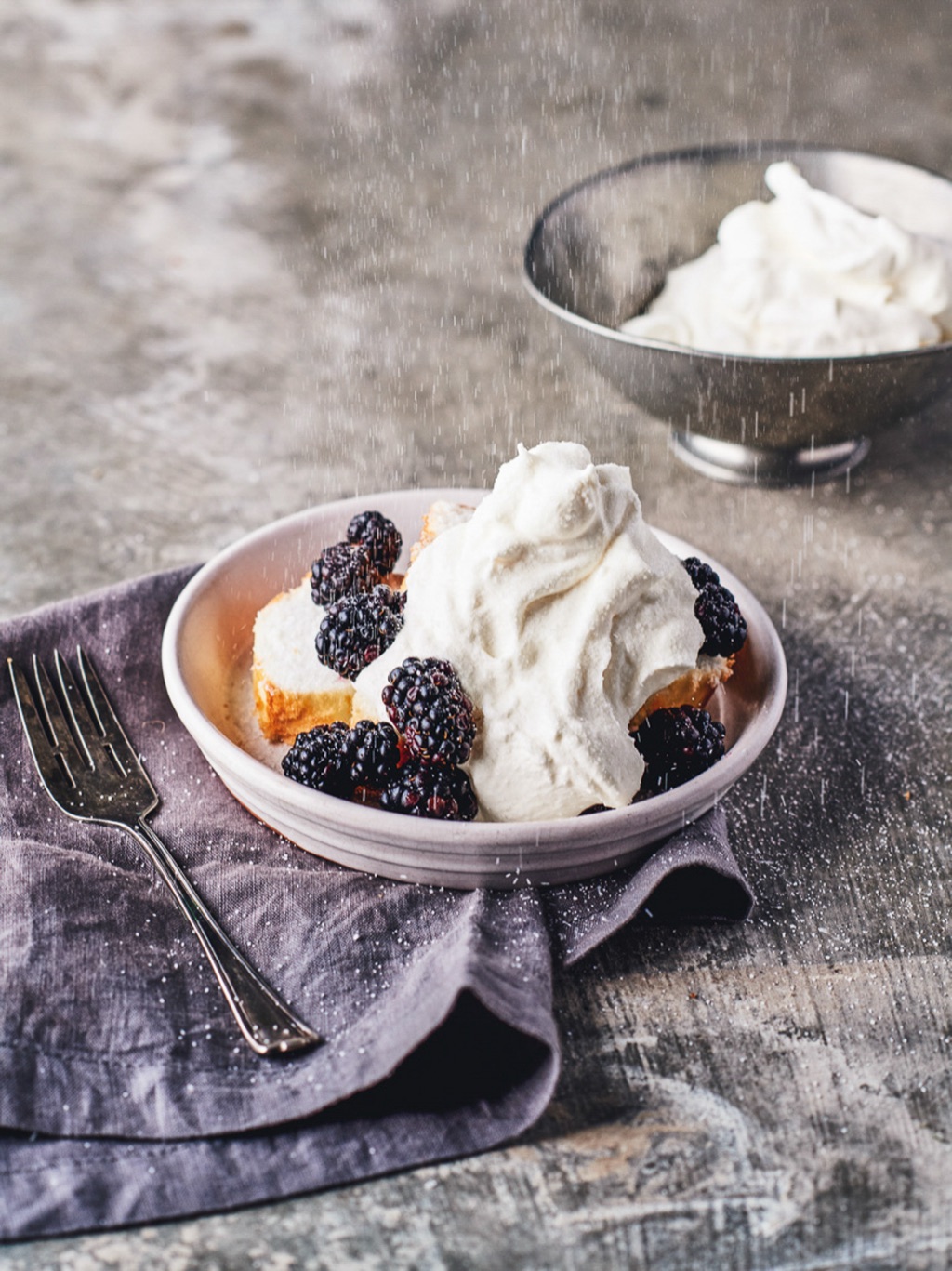 Angel food cake with blackberries and whipped cream as sugar sprinkles down
