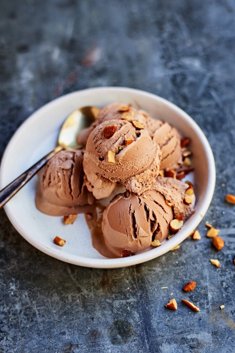 Bowl of chocolate ice cream scoops topped with chopped almonds and a gold spoon